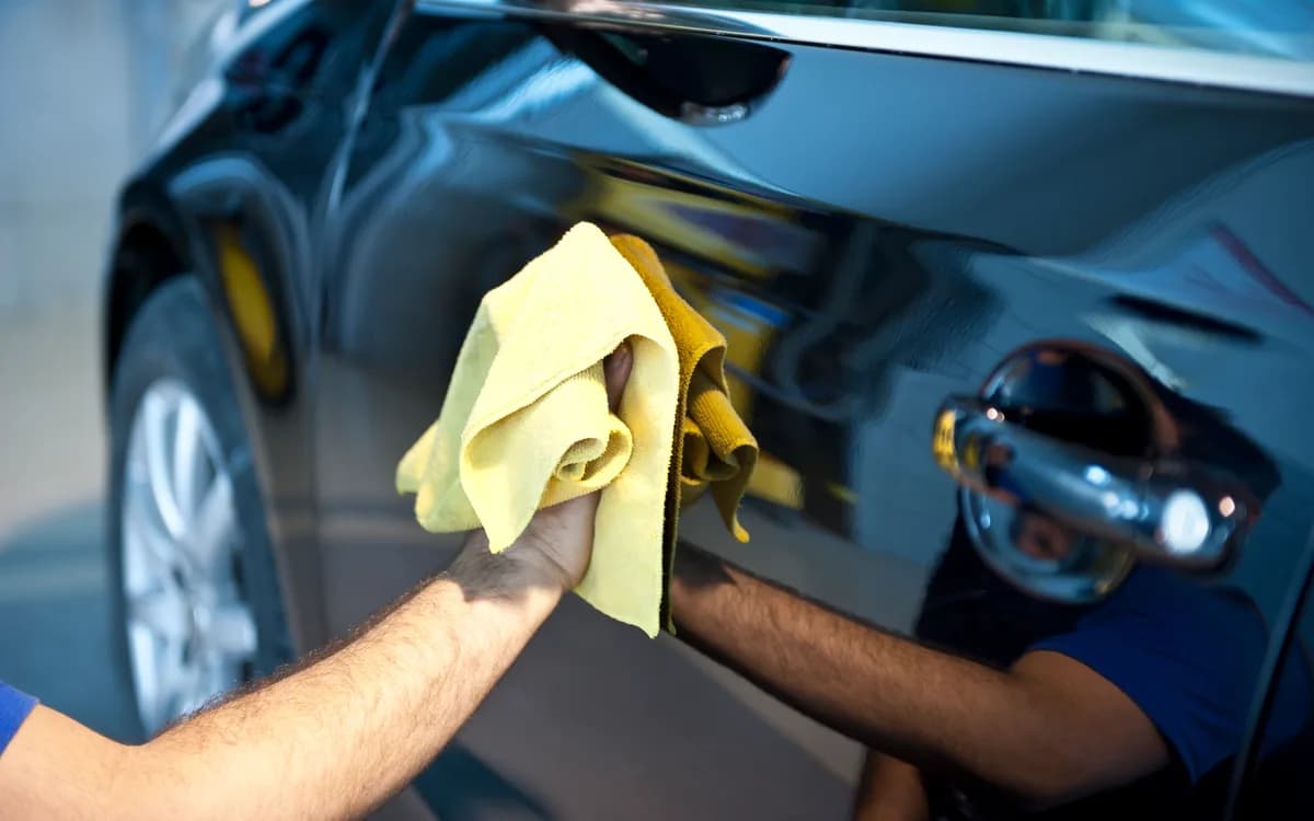 Dark car paintwork being polished with a microfibre cloth